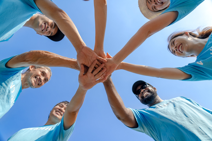 Group of happy diverse volunteers joining stacked hands together with smiles to show the power of unity in social environment charity working team, key success in making future a better world