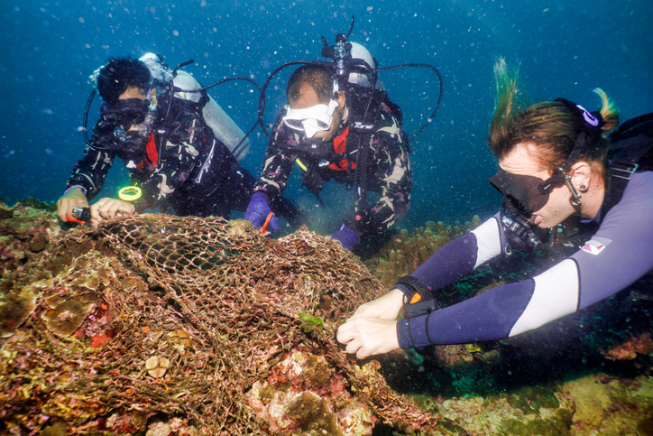 Three scuba divers underwater cleaning up nets and trash for Foundation For Humanity